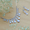 Silver necklace and earrings with clear gemstones on a beige background with small flowers.