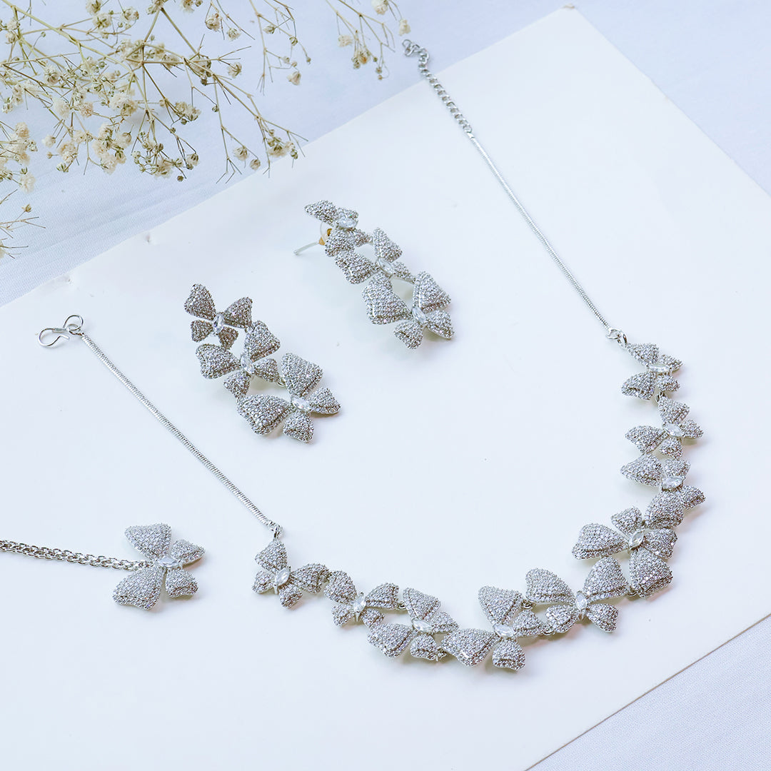 Silver butterfly necklace and earrings on a white surface with dried flowers.