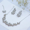 Silver necklace and earrings set on a white surface with dried flowers.