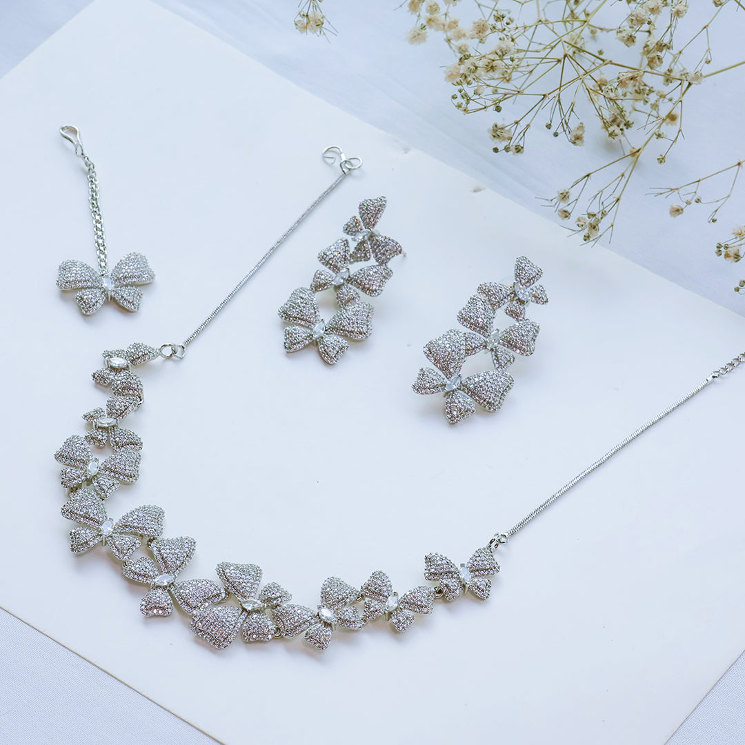 Silver necklace and earrings set on a white surface with dried flowers.