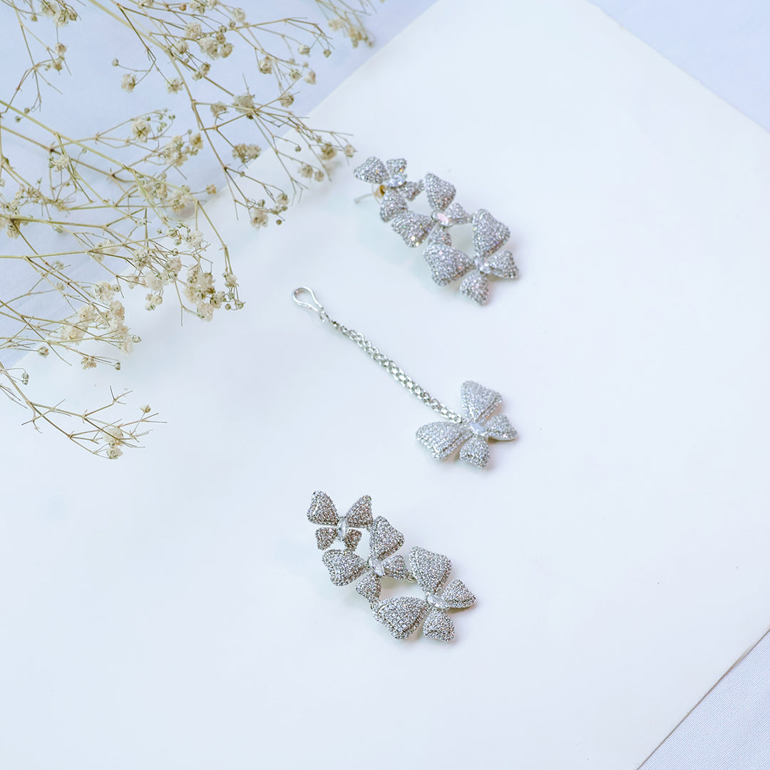 Silver bow-shaped earrings on a light surface with dried flowers.