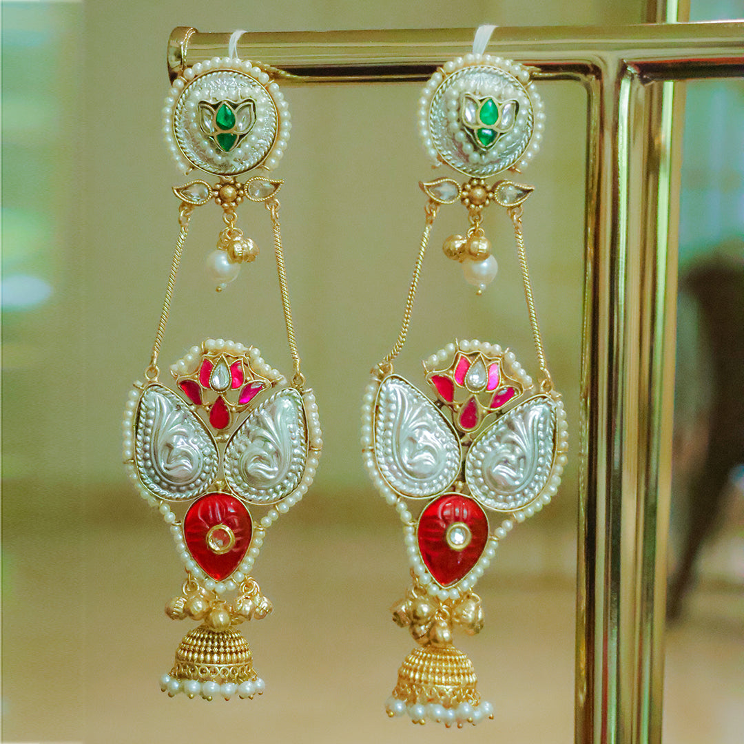Ornate earrings with red, green, and gold colors on a stand.