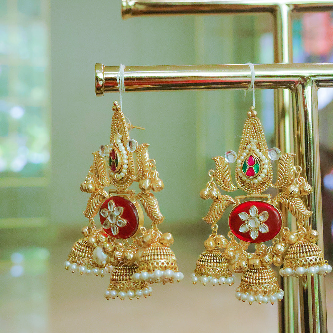 Ornate gold earrings with red centers on a gold stand.