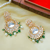 Pair of ornate gold earrings with pearls and green stones on a beige surface.
