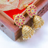 Gold and pink earrings on a wooden surface with a red fabric background