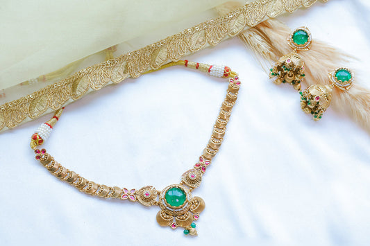 Gold necklace with green gemstones and matching earrings on a white background