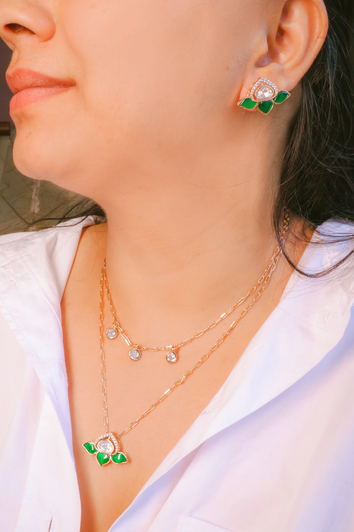 Close-up of a person wearing gold necklaces and earrings with green accents.