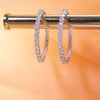 Diamond hoop earrings on a metallic stand with a blurred orange background