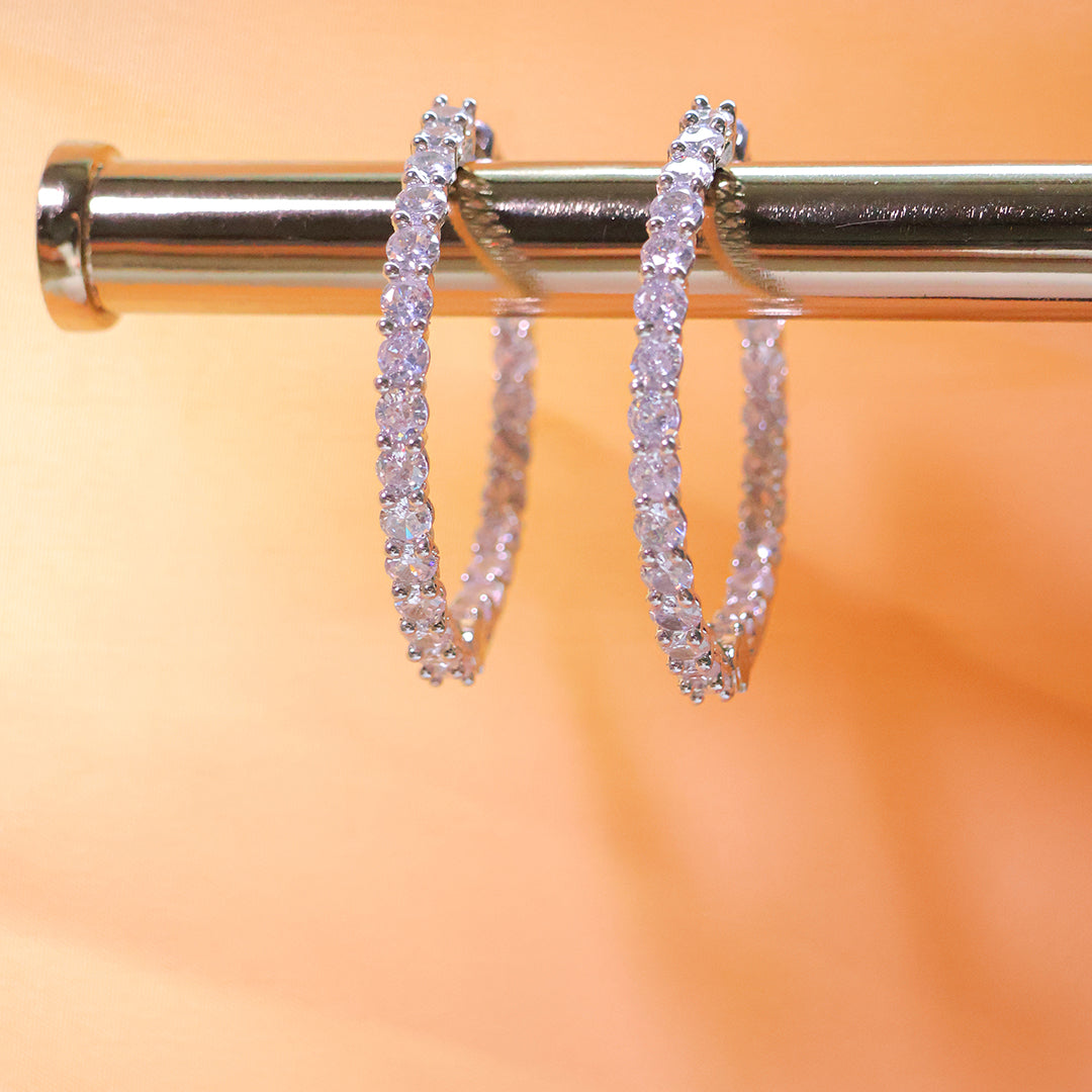 Diamond hoop earrings on a metallic stand with a blurred orange background
