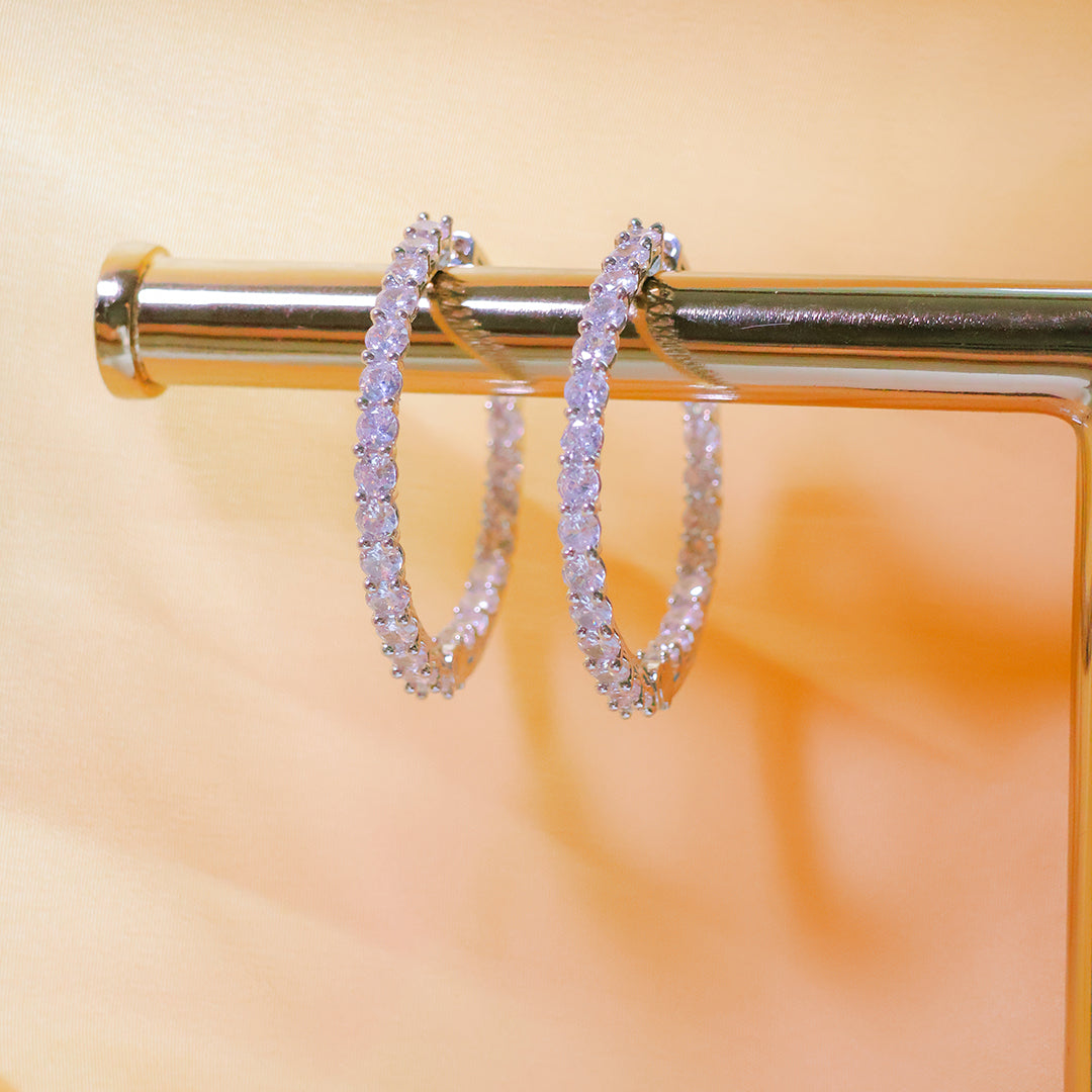 Pair of silver hoop earrings on a gold stand with a blurred orange background
