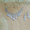 Silver necklace and earrings with clear stones on a beige background with small white flowers.